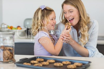 Girl feeding cookie to mother at counter