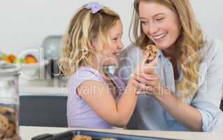 Girl feeding cookie to mother in kitchen