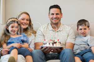 Family with cake sitting on sofa