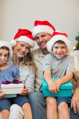 Family in Christmas hat holding presents on sofa