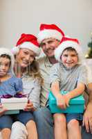 Family in Christmas hat holding presents on sofa