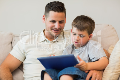 Father and son using digital tablet on sofa