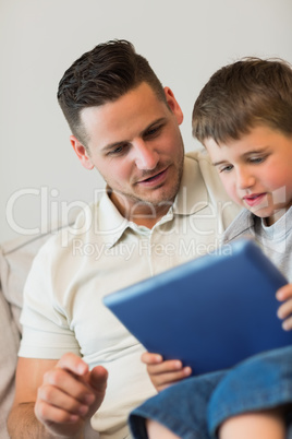 Father and son using tablet computer on sofa