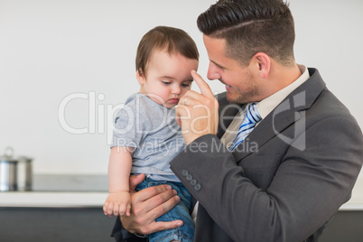 Businessman carrying baby boy in kitchen