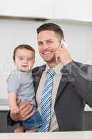Businessman carrying baby boy while on call