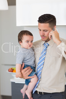 Businessman carrying baby boy while using mobile phone