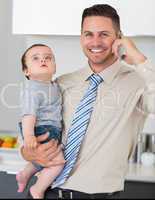 Businessman using cellphone while carrying baby in house