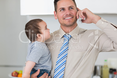 Businessman using mobile phone while carrying baby
