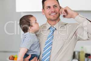 Businessman using mobile phone while carrying baby
