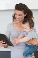 Mother looking at digital tablet while carrying baby