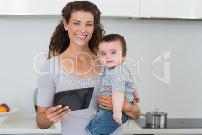 Mother carrying baby boy while holding digital tablet