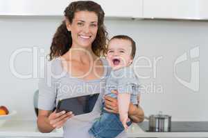 Happy mother with tablet carrying cheerful baby