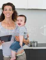 Mother with tablet computer carrying cheerful baby