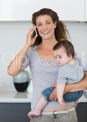 Happy woman answering smartphone while carrying baby