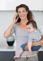 Happy woman answering smartphone while carrying baby
