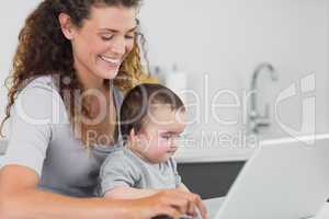 Smiling woman with baby using laptop