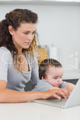 Woman with baby using laptop at counter