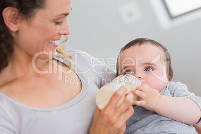 Smiling mother feeding milk to baby