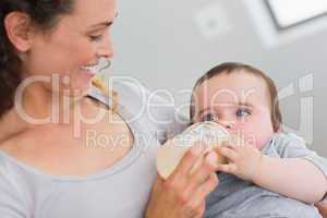 Smiling mother feeding milk to baby