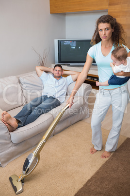 Young woman cleaning house while carrying baby