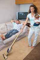 Young woman cleaning house while carrying baby