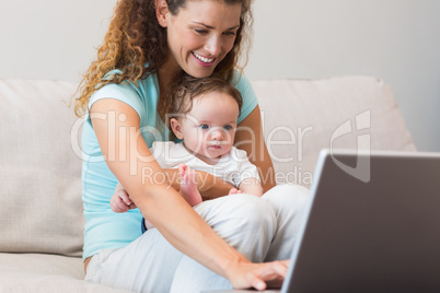 Mother using laptop while holding baby