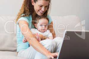 Mother using laptop while holding baby