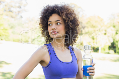 Thoughtful sporty woman holding water bottle