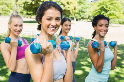 Happy multiethnic women lifting dumbbells