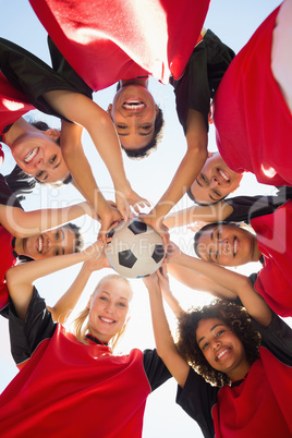 Soccer team with ball forming huddle against sky