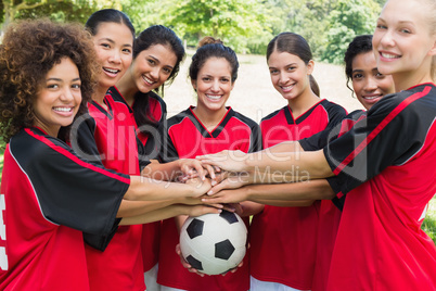 Confident soccer team stacking hands on ball