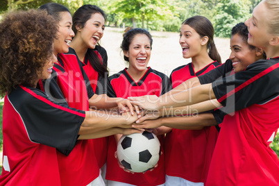 Excited soccer team stacking hands on ball