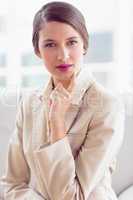 Thinking businesswoman sitting on sofa looking at camera