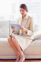 Thoughtful businesswoman sitting on sofa looking at tablet pc