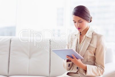 Stylish businesswoman sitting on sofa using tablet pc