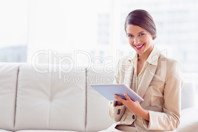 Stylish businesswoman sitting on sofa using tablet smiling at ca
