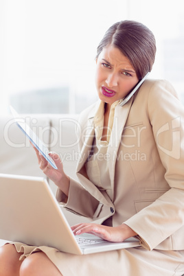 Busy and stressed businesswoman sitting on sofa multi tasking