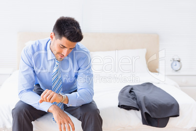 Handsome businessman sitting on bed checking the time