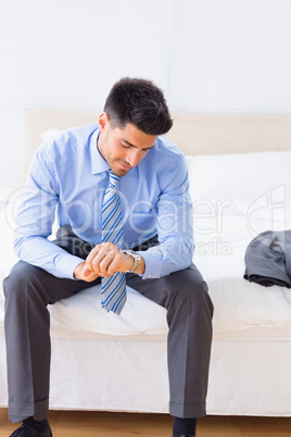 Attractive businessman sitting on bed checking the time