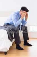 Hungover businessman sitting at edge of bed