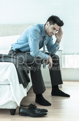 Wincing businessman sitting at edge of bed