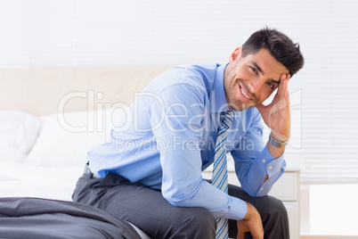 Cheerful businessman sitting at edge of bed looking at camera