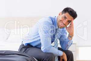 Cheerful businessman sitting at edge of bed looking at camera