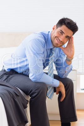 Happy businessman sitting at edge of bed looking at camera