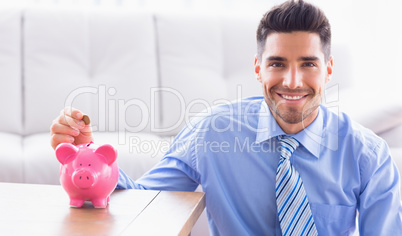 Happy businessman putting coins into piggy bank