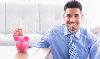 Happy businessman putting coins into piggy bank
