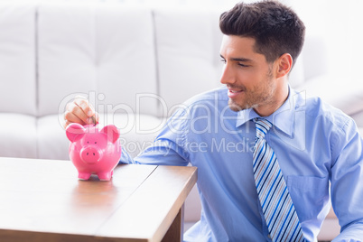 Smiling businessman putting coins into piggy bank