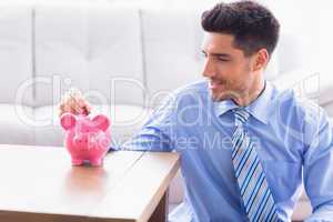 Smiling businessman putting coins into piggy bank