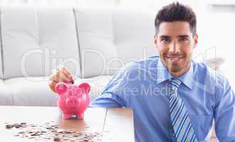 Cheerful businessman putting coins into piggy bank