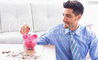 Handsome businessman putting coins into piggy bank